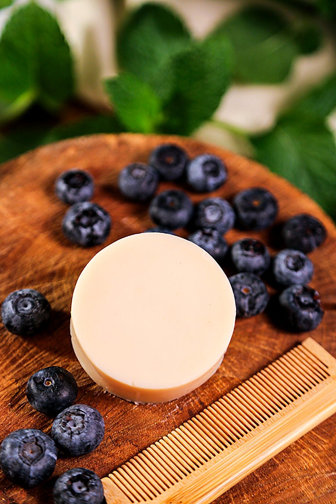 Condicionador em barra Blueberry da Olga Biocosméticos sobre madeira, com mirtilos, folhas de hortelã e pente de bambu