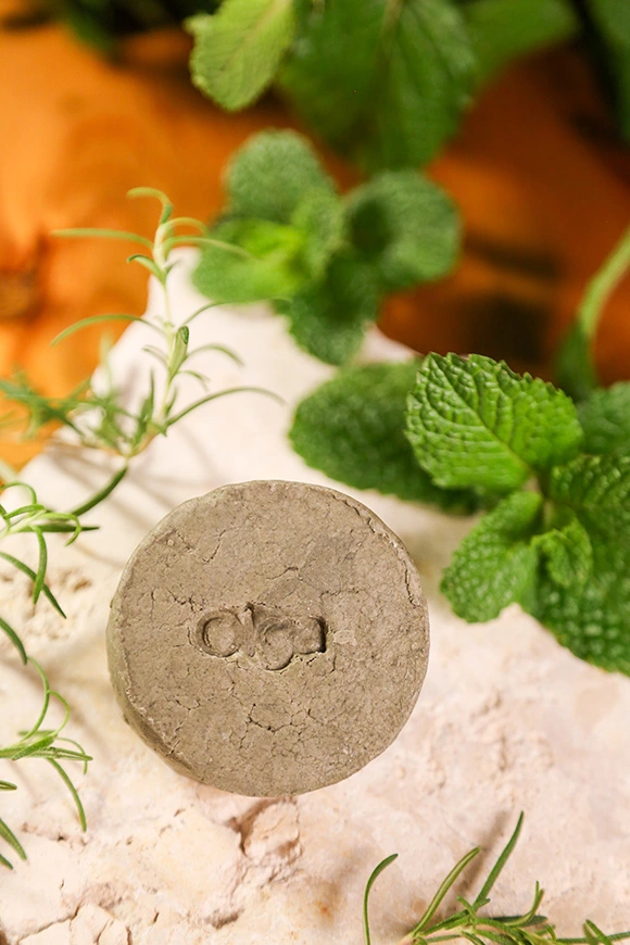 Shampoo sólido em barra Olga de Alecrim, Menta e Jaborandi sobre pedra natural, com ramos frescos de alecrim e folhas de menta ao redor.